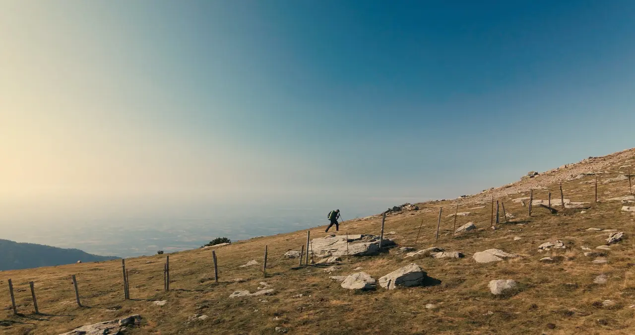 Un marcheur seul sur une crête d’herbe sèche, au-dessus d’une mer de nuages.